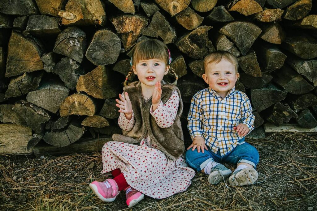 baby and toddler sitting in front of wood rounds during portrait session in the fall at Martis Camp