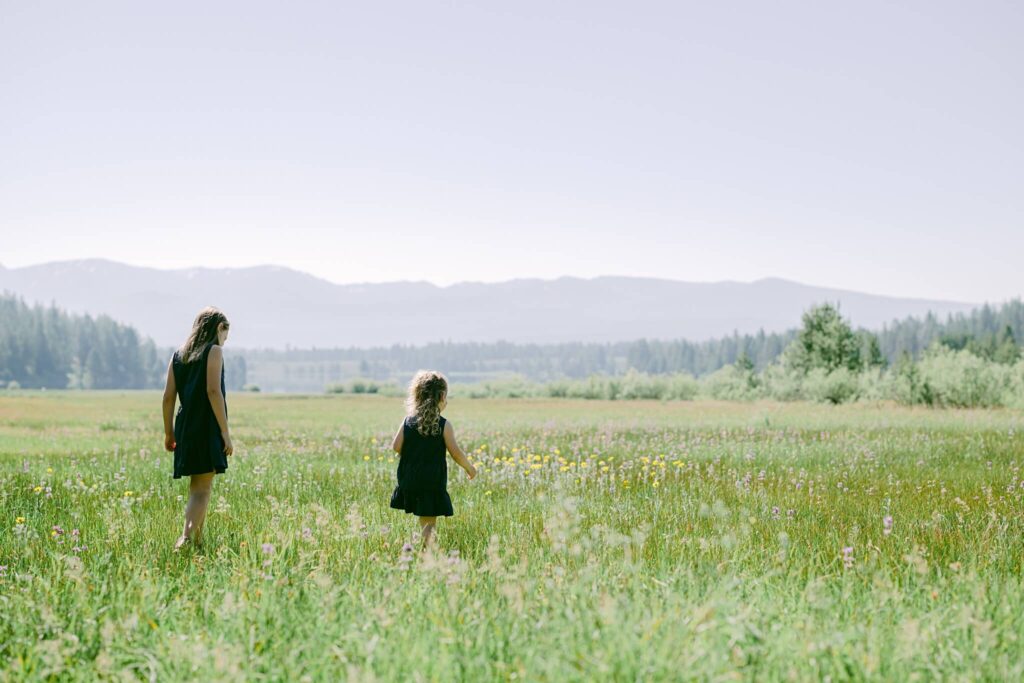 young sisters in navy dresses walking in a field of flowers in a Truckee meadow captured by Annie X Photographie