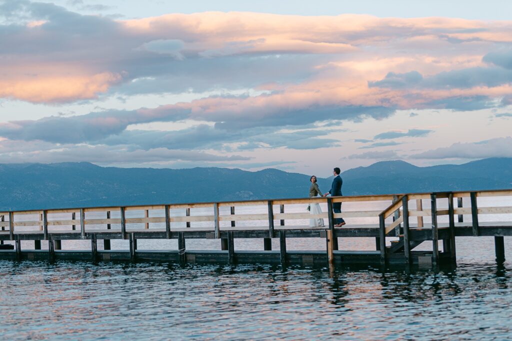 Bride and Groom walking at sunset with pink clouds on a pier in Lake Tahoe