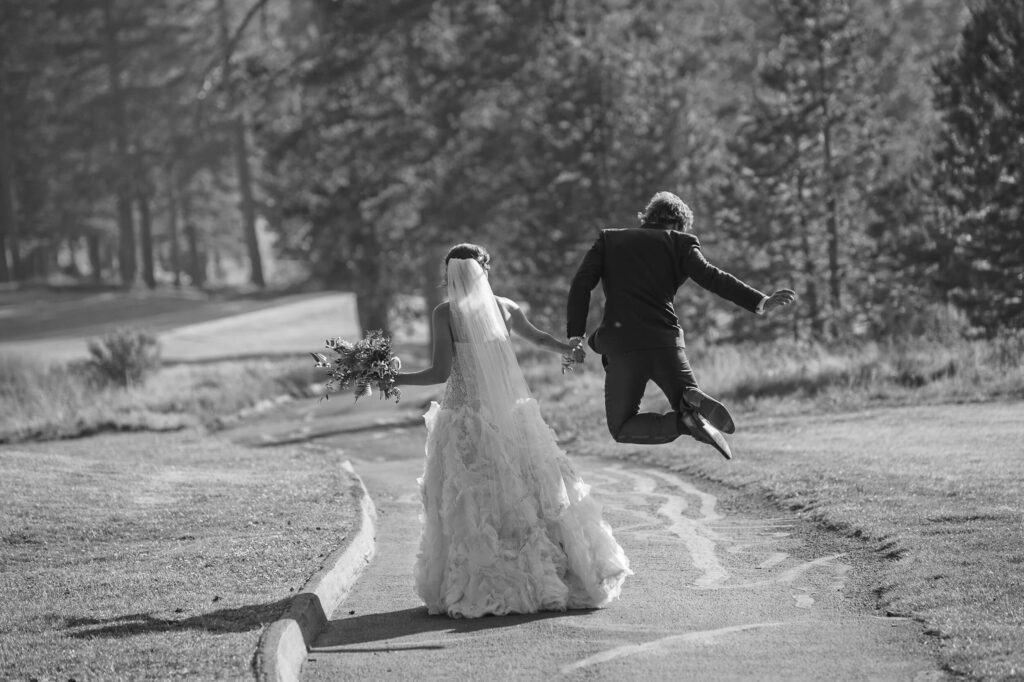 Couple of Newlyweds walking on path with groom jumping in the air surpriging his bride , candid capture with Annie X Photographie
