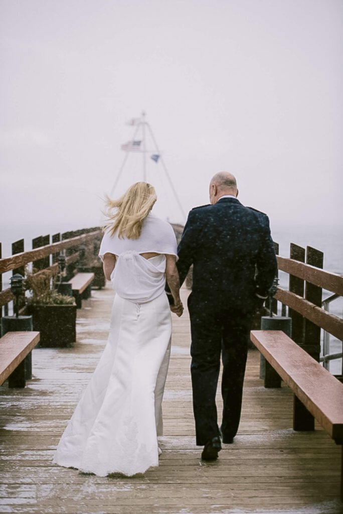 Bride and Groom walking on the Gar Woods pier after their ceremony with snowy skies and wind.