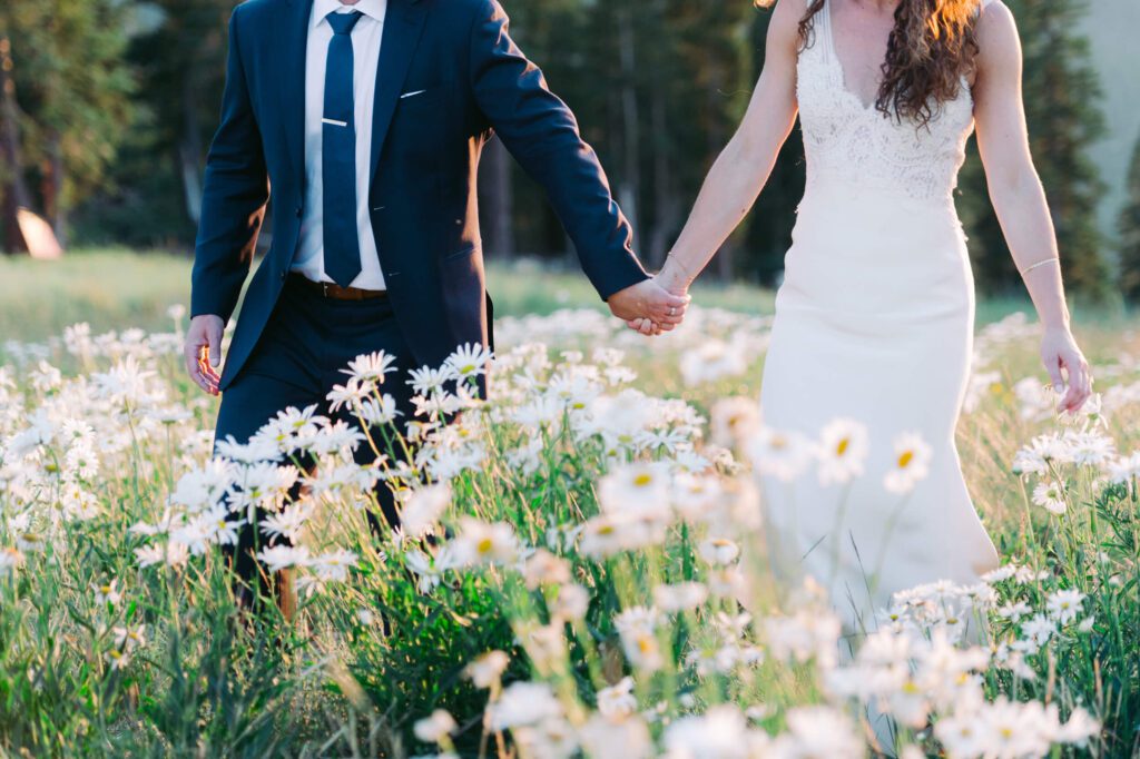 close up of hands of a braide nad groom in a field of daisies Northstar wedding up at the Zephyr lodge