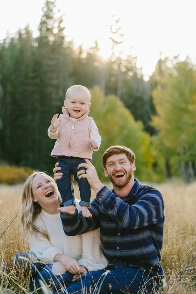 young parents laughing and holding their toddler up during fall family session