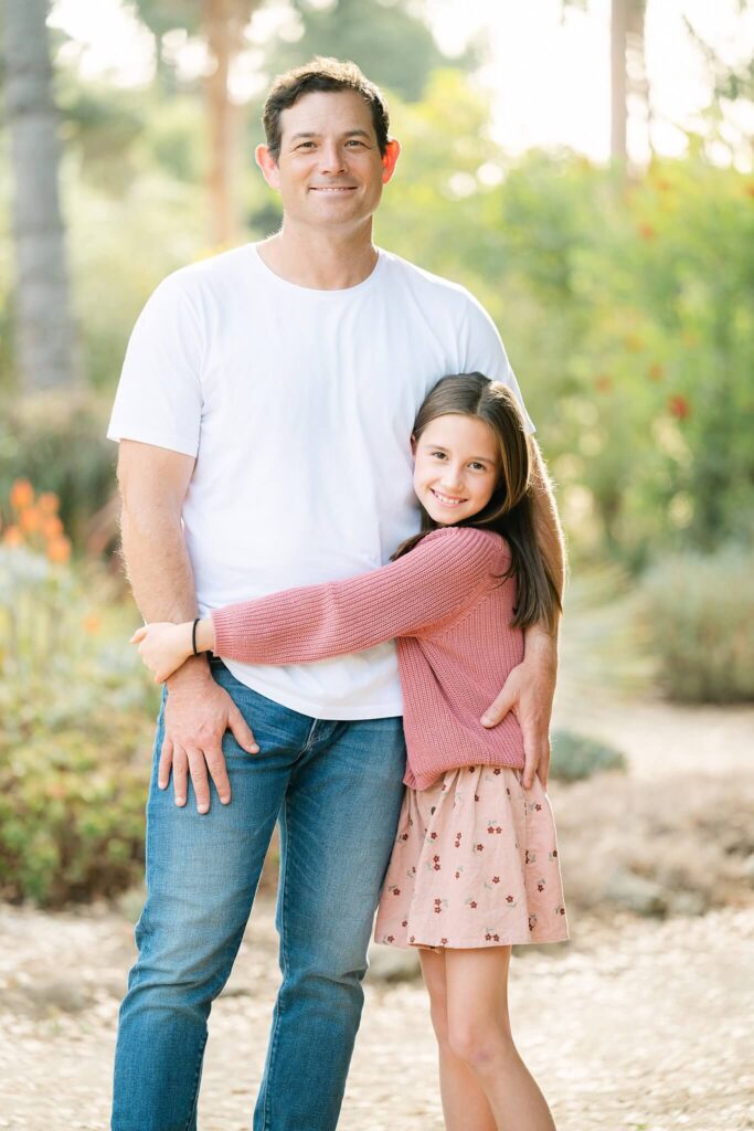 a dad and her girl facing camera as she is hugging him