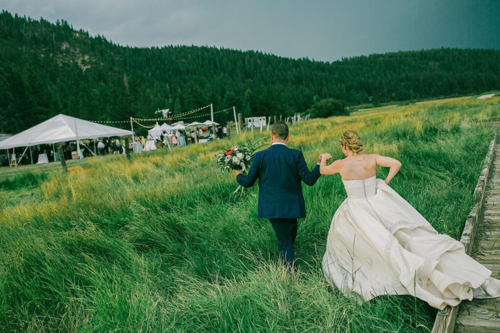 Bride and Groom walking towards their reception site through the tall grass during an end of summer wedding at the Stables at Palisades Tahoe