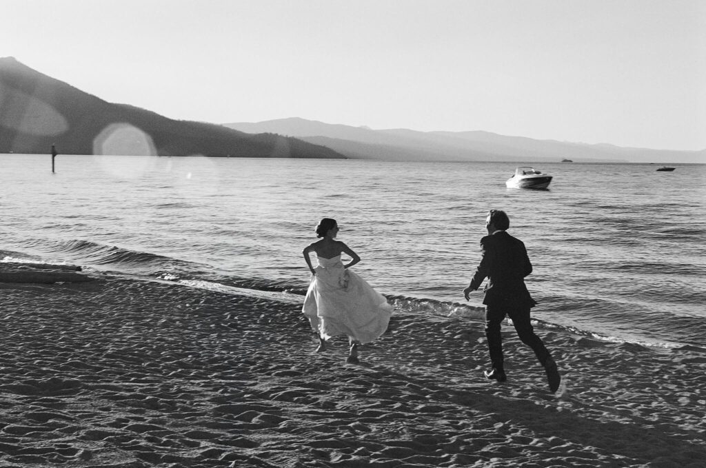 Black and white film image of bride and groom running on teh beach of their private Lake Tahoe lakefront estate