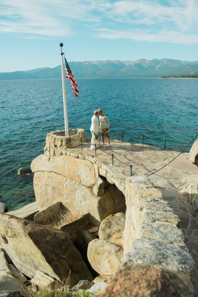 Two Brides kissing at the end of a lakefront walkway and flag over Lake Tahoe at this Lake Tahoe lakefront wedding venues the Thunderbird Lodge