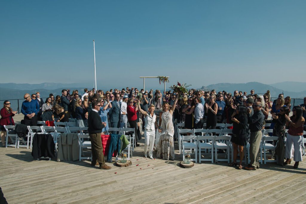 two brides just married up at High Camp at their ceremony just married vibe walking end of ceremony aisle with their guests