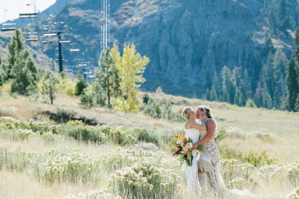 two brides kissing in tall grasses on the face of KT-22 where they ski during winter at Palisades Tahoe