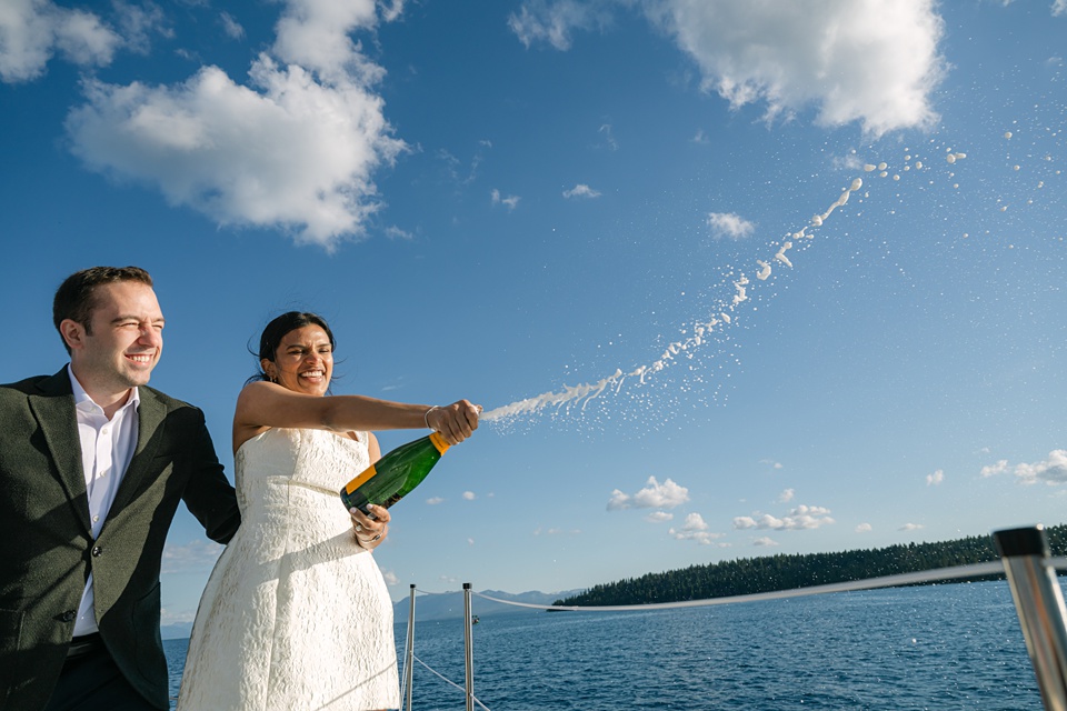 Tahoe City wedding photographer capturing couple on Sierra Cloud catamaran popping champagne during their golden hour cruise