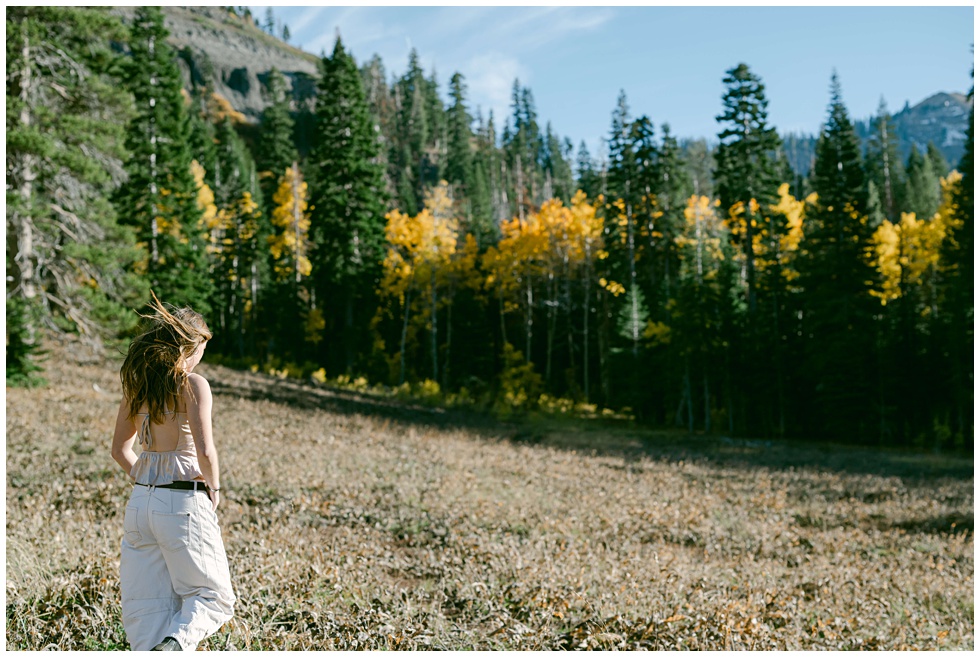 Tahoe senior photographer captures girl walking towards aspen trees and mountain backdrop during windy photo session