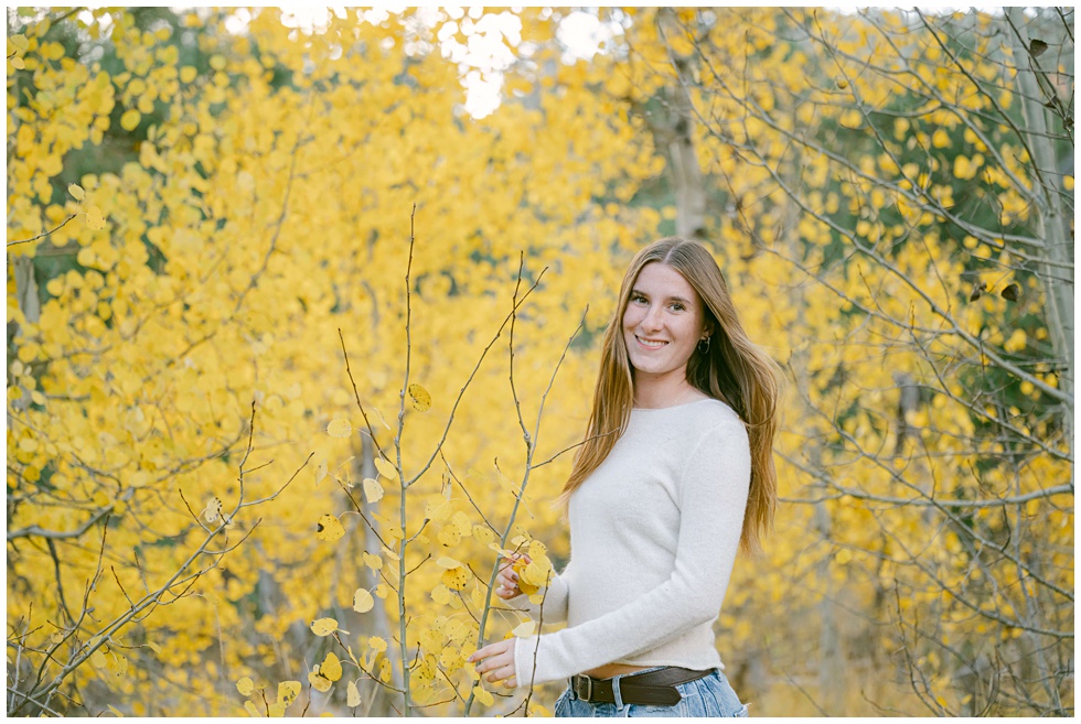 Stunning Fall Senior Photos in the Mountains with girl cream sweater and jeans with full yellow foliage in the back captured by Annie X Photographie