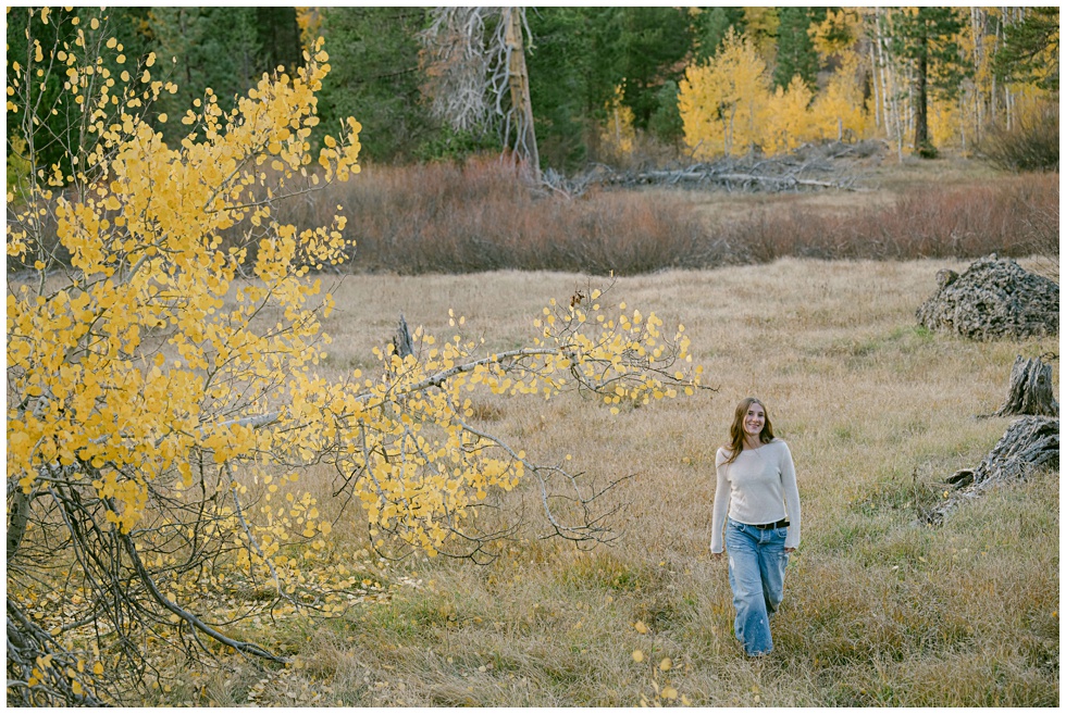 fall senior photos in Tahoe of a senior girl in cream sweater and jeans view from far in a meadow during fall