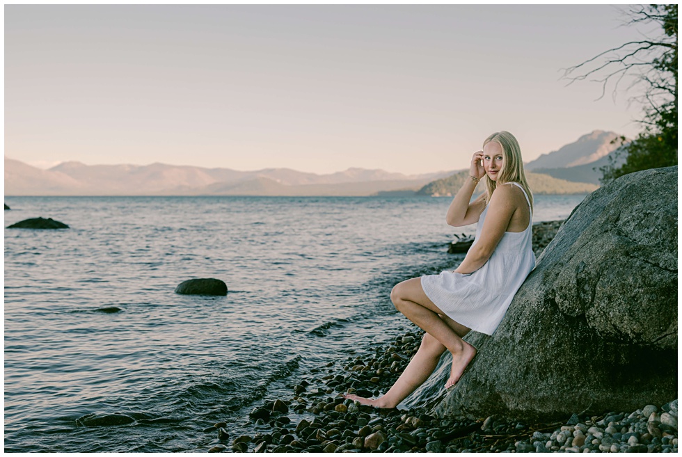 Tahoe senior portraits of blond girl sitting on boulder on the pebbled  beach of lake tahoe at sunset
