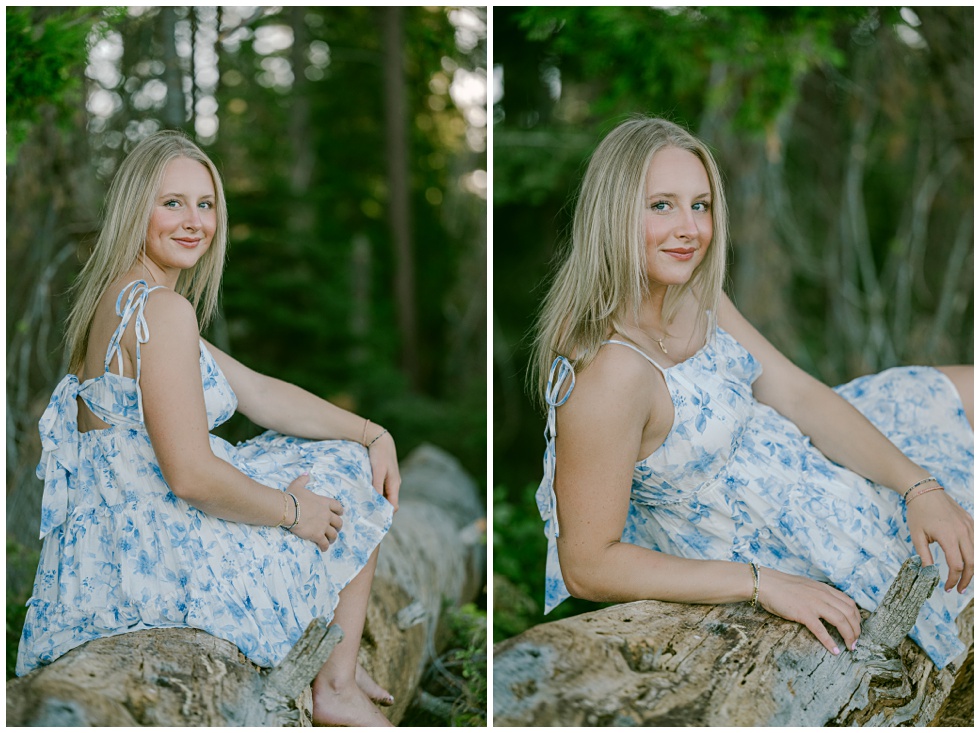Senior portrait surrounded by forest light sitting on a tree stump looking at camera
