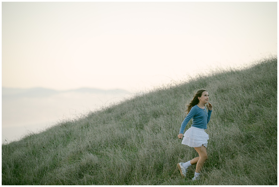 Candid portrait of girl running in tall golden grass during a photo session in marin captured by marin family photographer Annie X Photographie