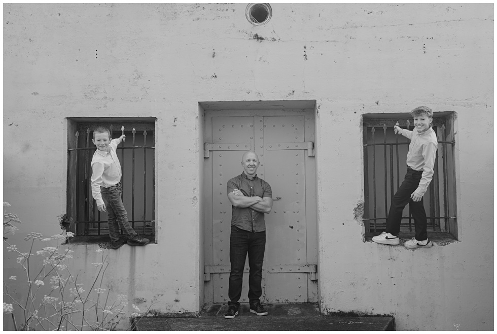 Black and white portrait of father and his two sons in playful pose in front of bunkers in Sausalito captured during a PT Cavallo family session