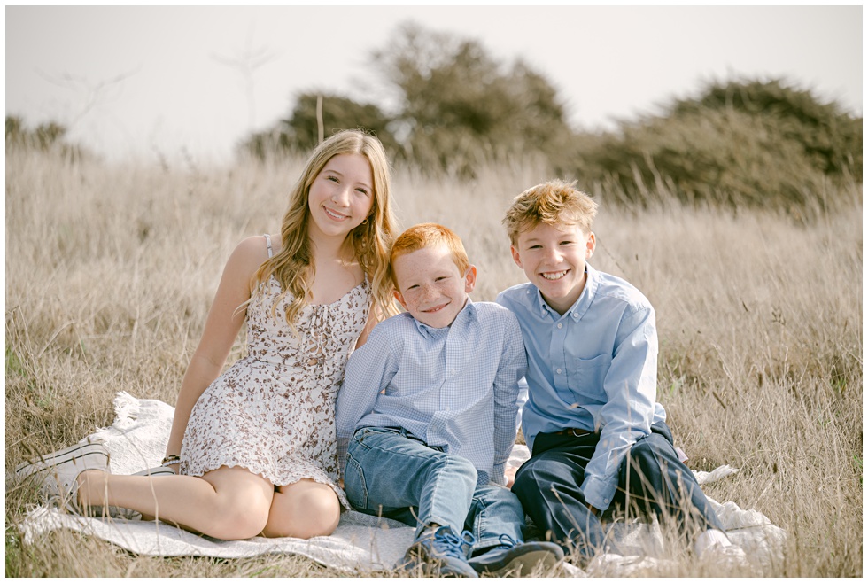 Natural family photo cof teh kids sitting in tall golden grass captured in Sausalito by Annie X Photographie