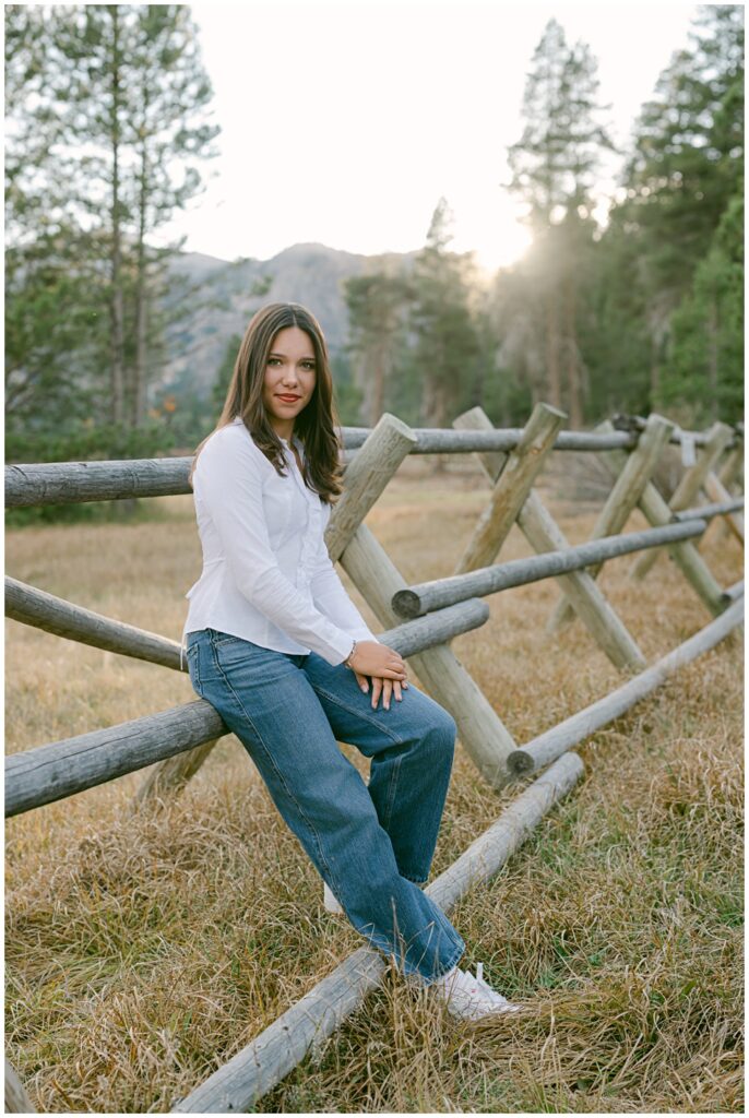 Senior girl leaning on wooden fence with fall light in Olympic Valley
