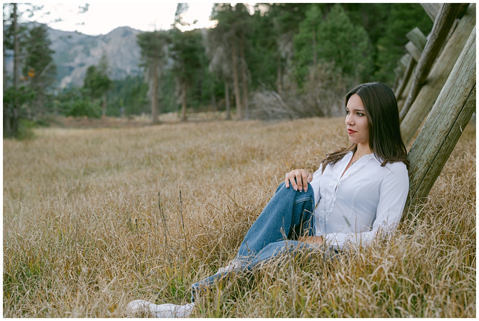 Editorial style senior portrait in Olympic Valley with golden light sitting at iconic Palisades fence