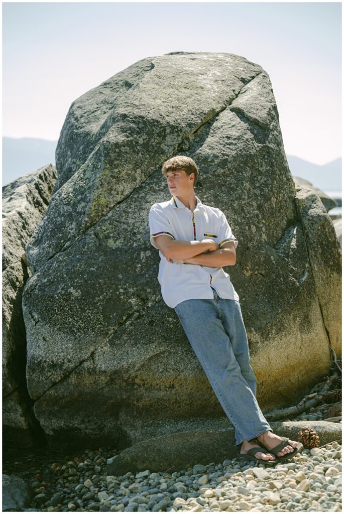 Senior boy on lakeshore rock with Tahoe blue behind him