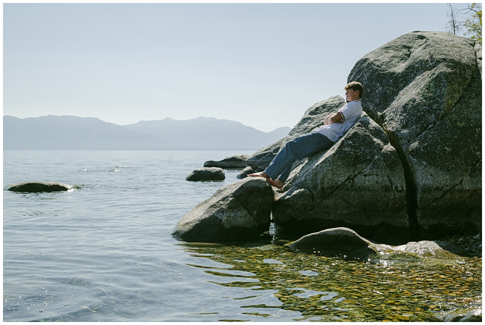 Environmental senior portrait at Sugar Pine Point with calm morning light boy leaning on granite rocks in Lake tahoe looking out