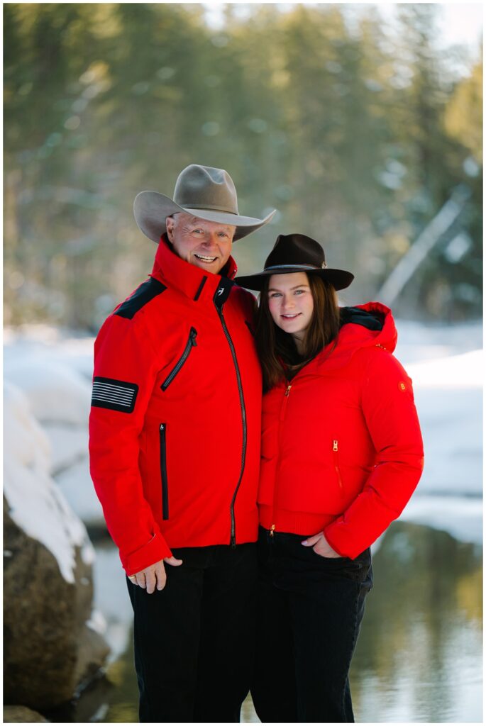 Dad and daughter smiling at camera wearing red jackets and both with cowboy hats at Donner memorial park in winter