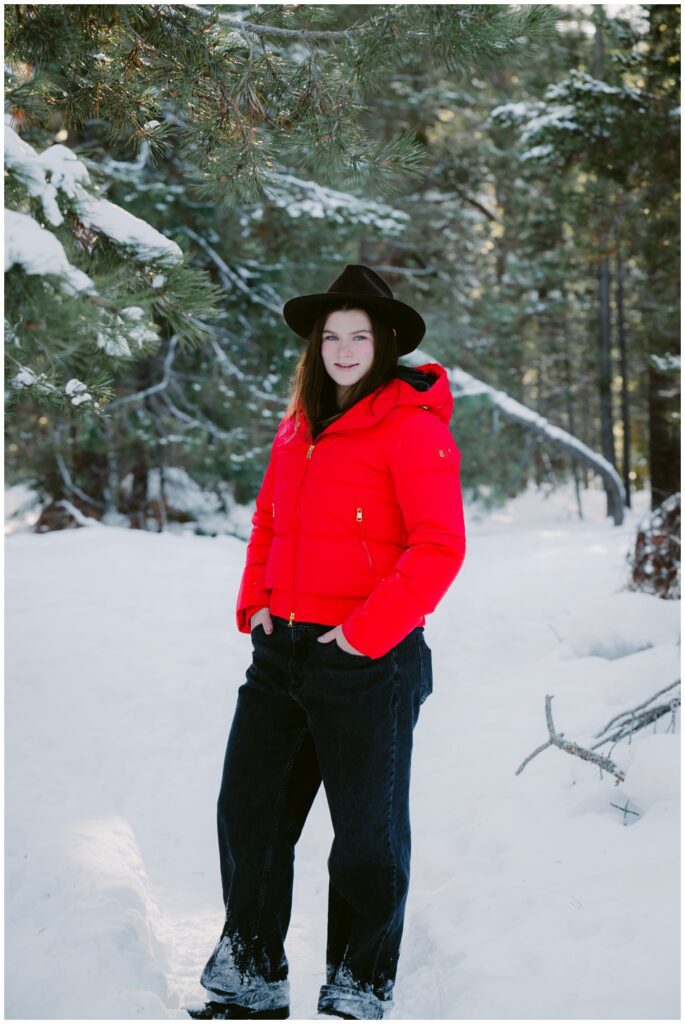 young woman wearing red winter jacket and black cowboy hat full length in snow