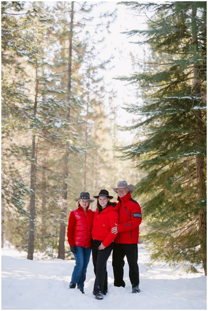 Parents hugging their daughter in the snow during a winter family session.