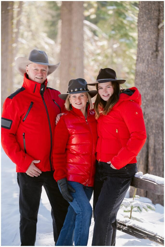 Family standing among tall pines with clean white snow,  wearing red jackets during a short winter photo session in Truckee for their Valentine's card