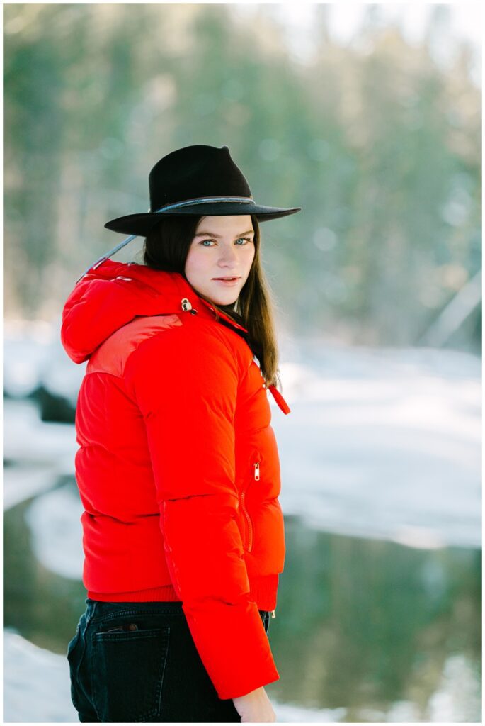 Girl in a red winter coat and black cowboy hat looking back at camera in winter captured by Tahoe family photographer Annie X Photographie
