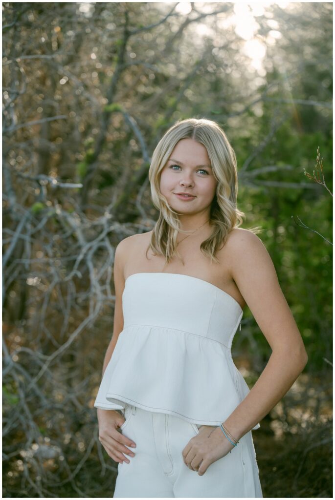 Lake Tahoe senior portraits editorial close up of Truckee High School senior in white strapless peplum top with confident direct gaze and bare winter branches bokeh background Sugar Pine Point spring session
