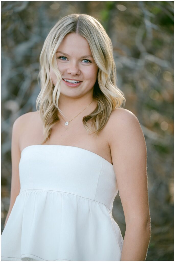 Truckee senior photographer senior in white peplum top and wide leg jeans on rocky Lake Tahoe shoreline with bare winter brush and soft lake light Sugar Pine Point