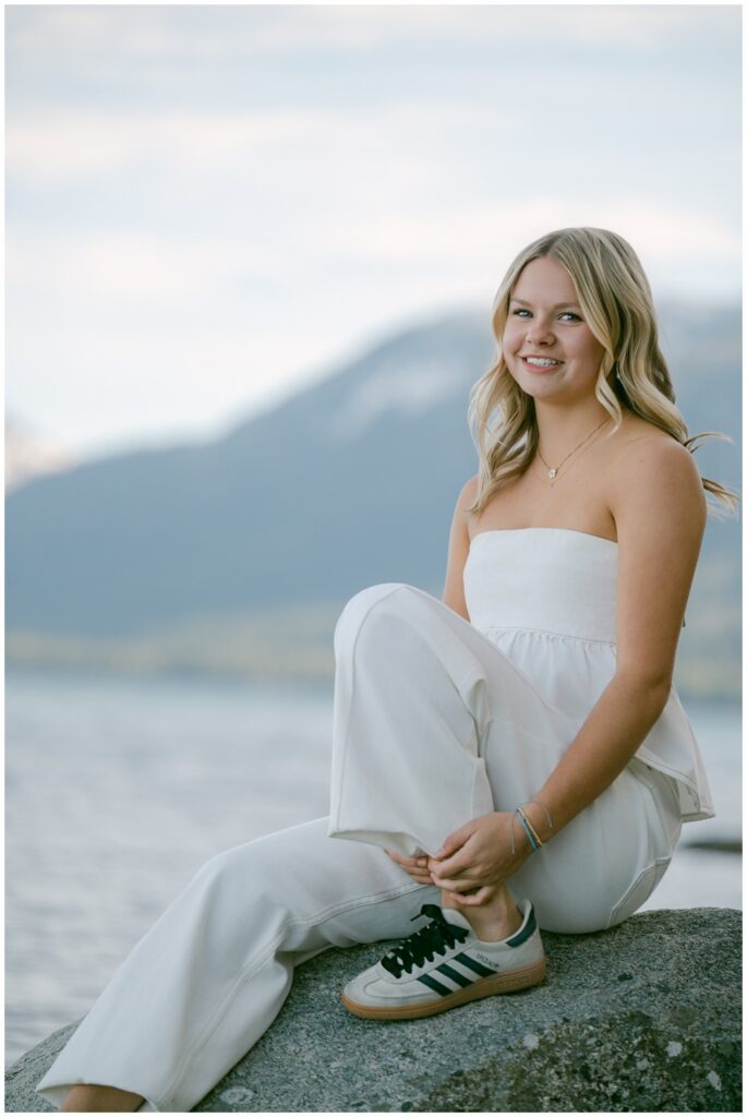 Lake Tahoe senior portraits candid portrait of Truckee High School senior in white outfit sitting on granite rock with soft mountain and lake backdrop Sugar Pine Point West Shore