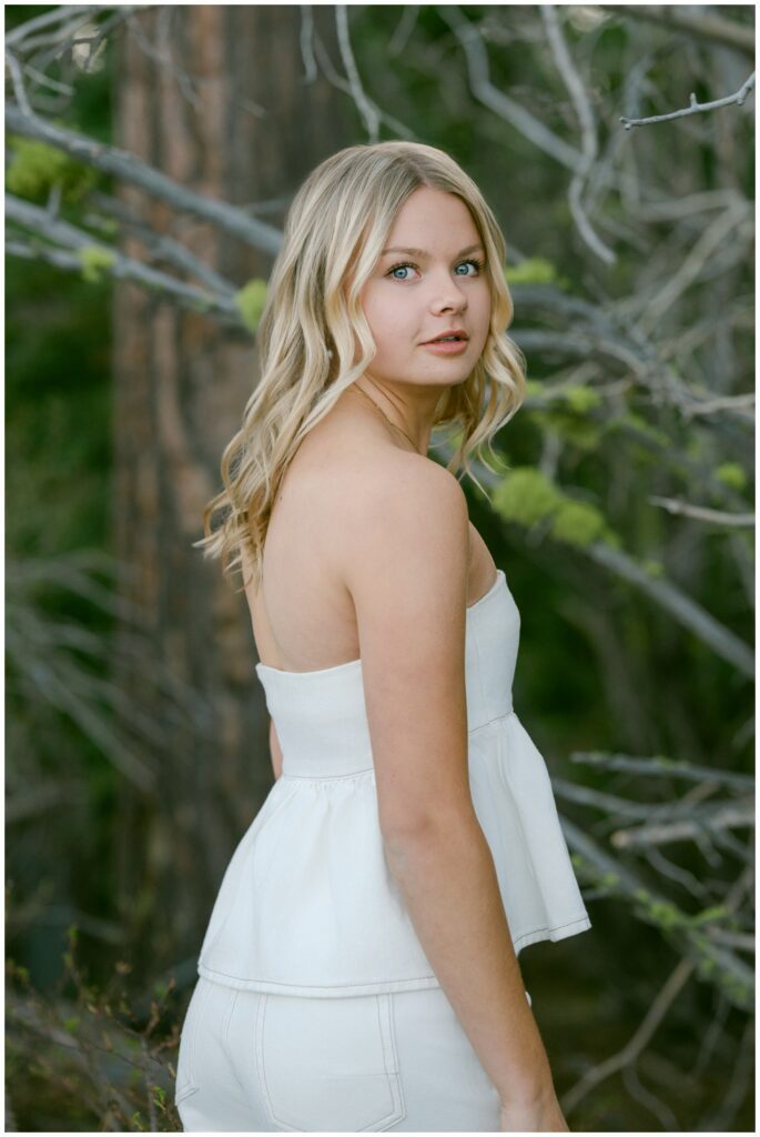Truckee senior photographer over the shoulder portrait of Class of 2026 senior in white tonal outfit with spring budding green foliage Sugar Pine Point State Park West Shore spring session