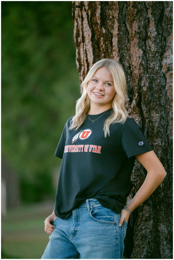 Lake Tahoe senior photos Truckee High School senior in University of Utah shirt and jeans leaning on ponderosa pine tree with green forest bokeh Sugar Pine Point spring session college commitment portrait