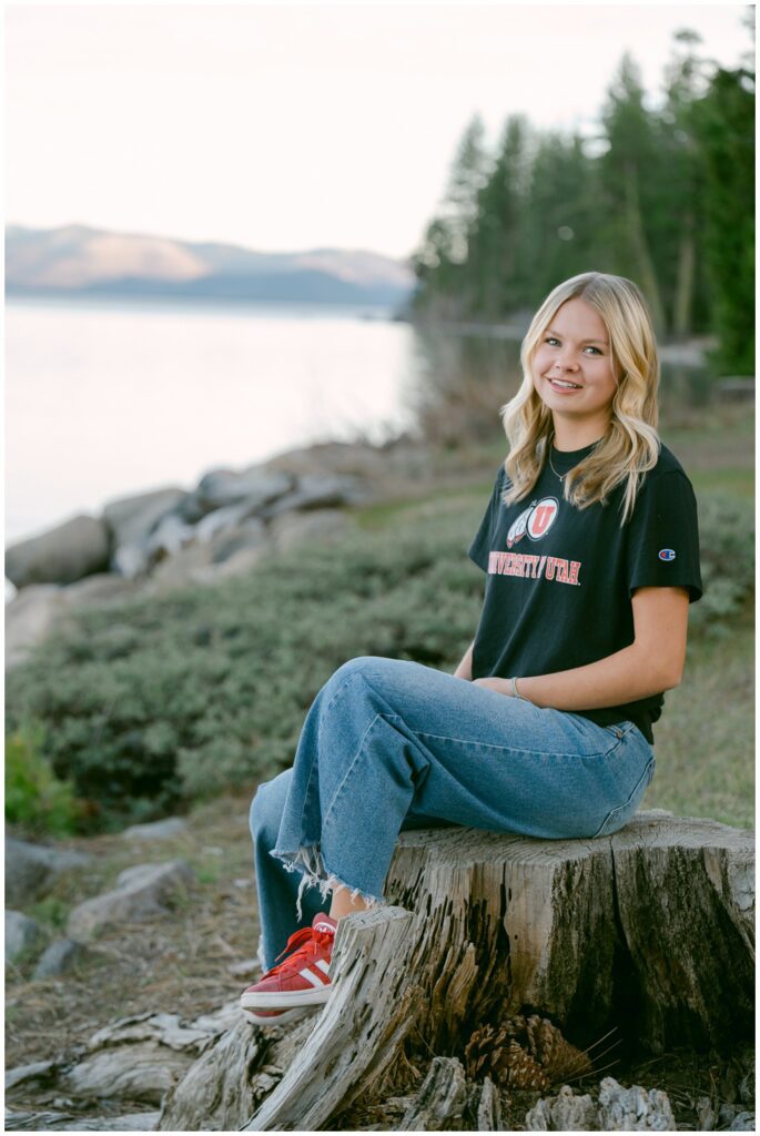 Truckee senior photographer Truckee High School Class of 2026 senior in University of Utah shirt and red Adidas Sambas sitting on driftwood stump at Lake Tahoe West Shore lakeside at dusk Sugar Pine Point