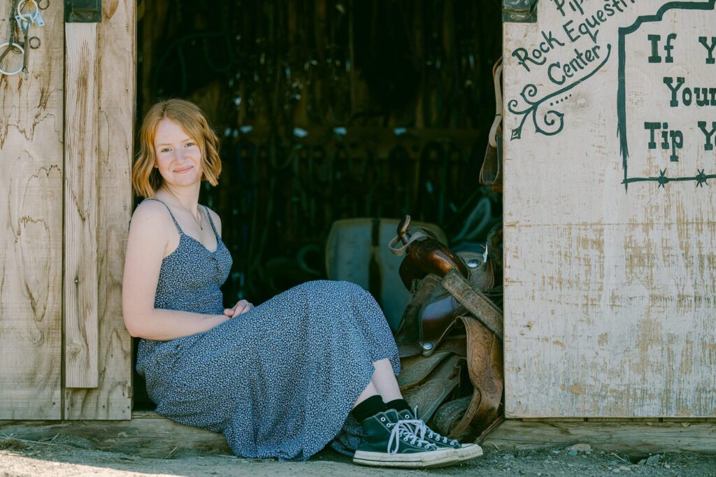 red haired senior girl sitting in door of barn at piping rock in truckee