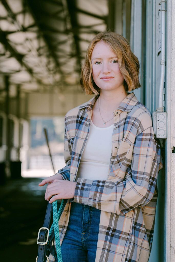 Senior girl wearing plaid shirt outside a barn looking at camera with red hair bob